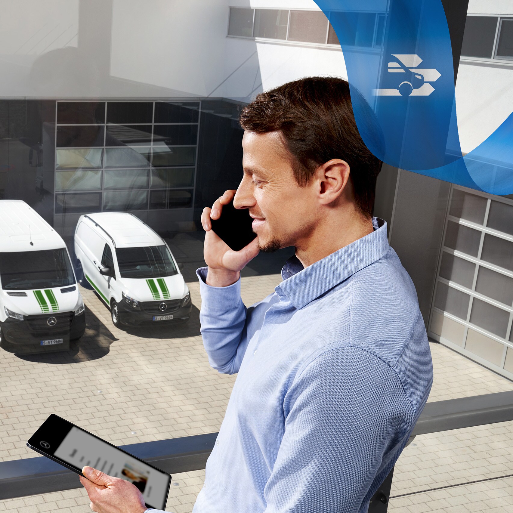 Een man telefoneert terwijl hij naar een tablet kijkt, met een reeks Mercedes-Benz bestelwagens op de achtergrond.