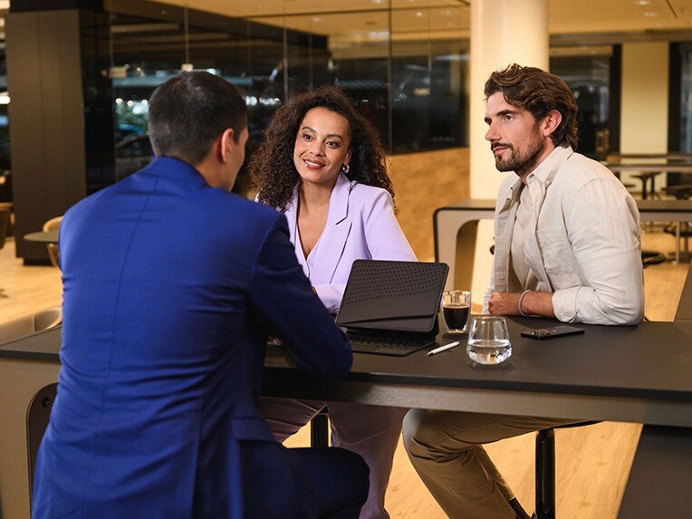 Drie personen zitten aan een tafel en zijn in gesprek.