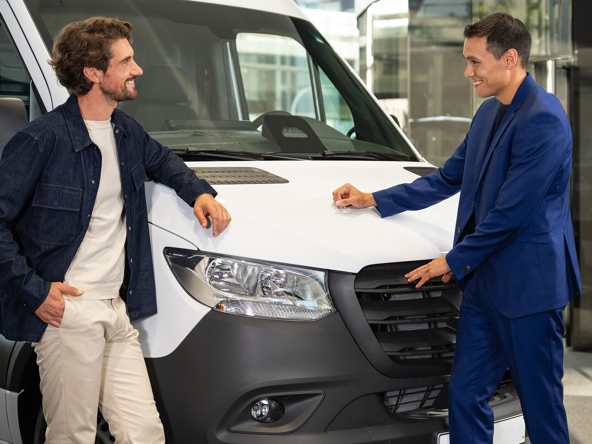 Twee personen leunen tegen een Mercedes-Benz bestelwagen en zijn in gesprek.