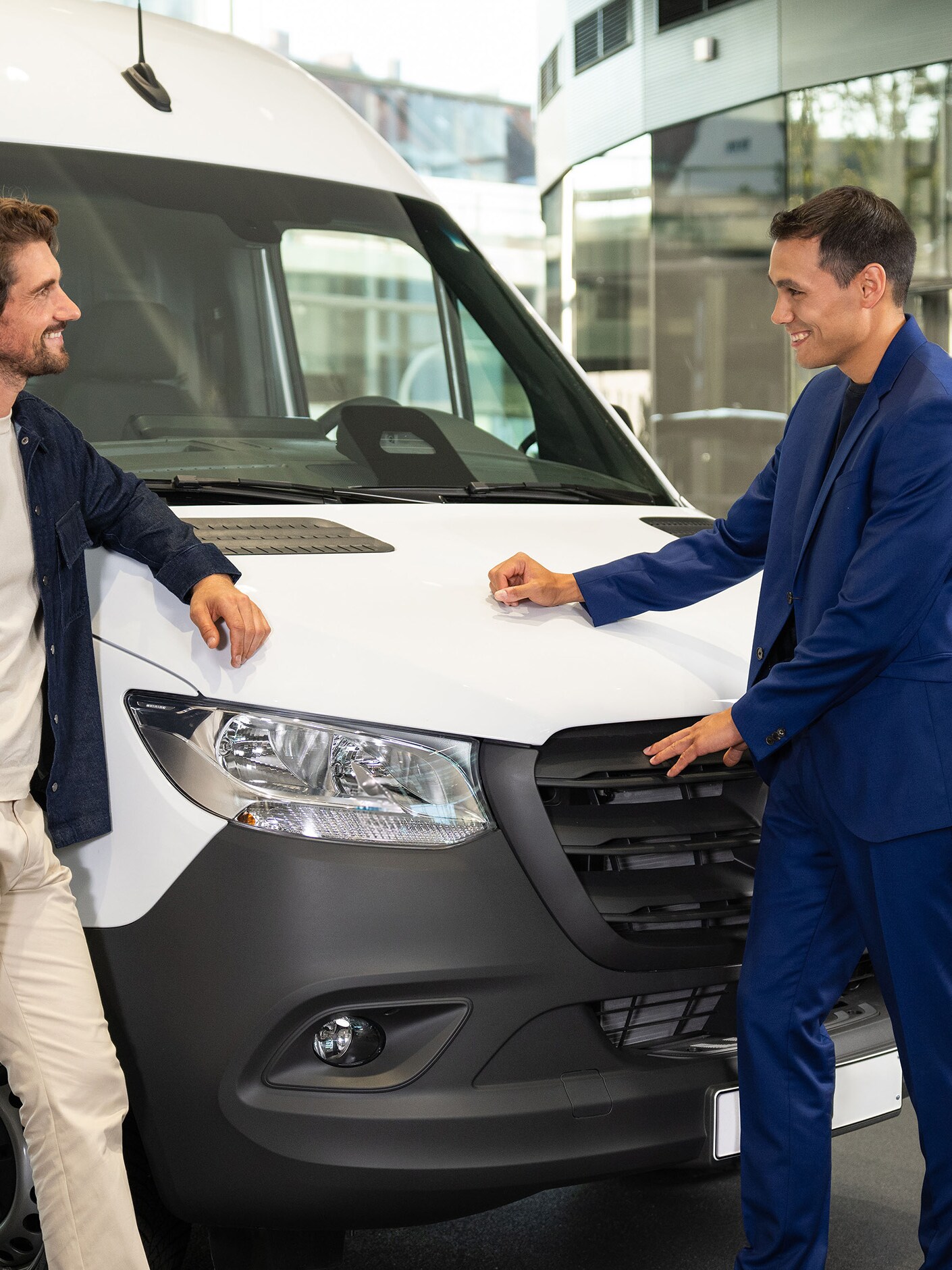 Twee personen leunen tegen een Mercedes-Benz bestelwagen en zijn in gesprek.