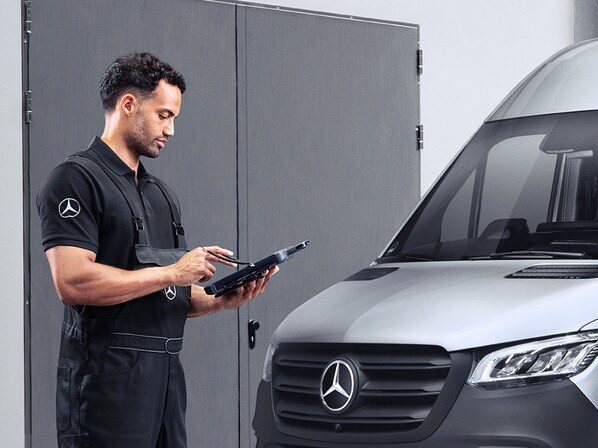 Een Mercedes-Benz technicus knielt voor een auto en voert de periodieke keuring uit.